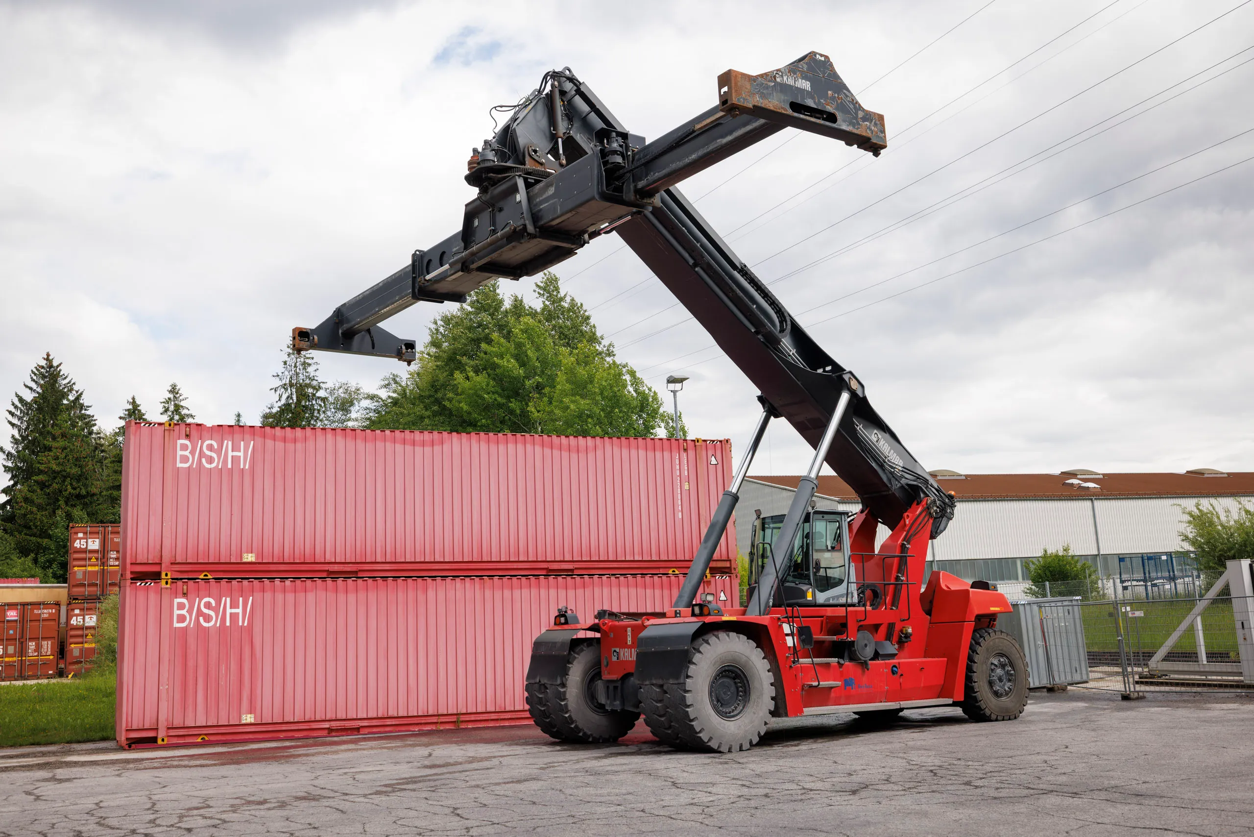 Ein roter Container Stapler steht vor zwei roten BSH Container. Es ist bewölkt.