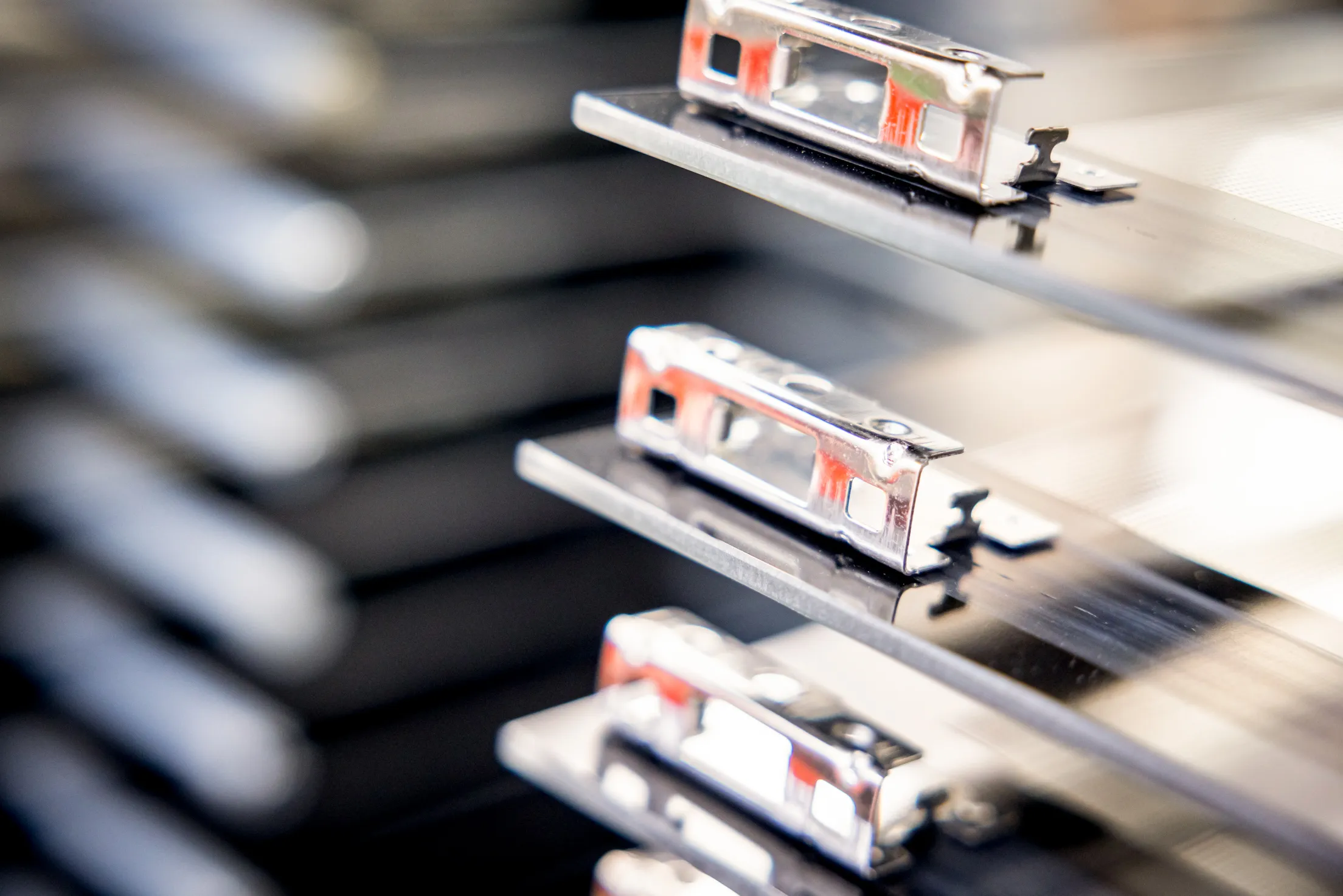 Detail von mehreren Ofentüren und Scharnieren. Alles im Foto ist unscharf in Grautönen und mit etwas Orange. Der Fokus liegt auf einem Scharnier, welches scharf abgebildet ist.