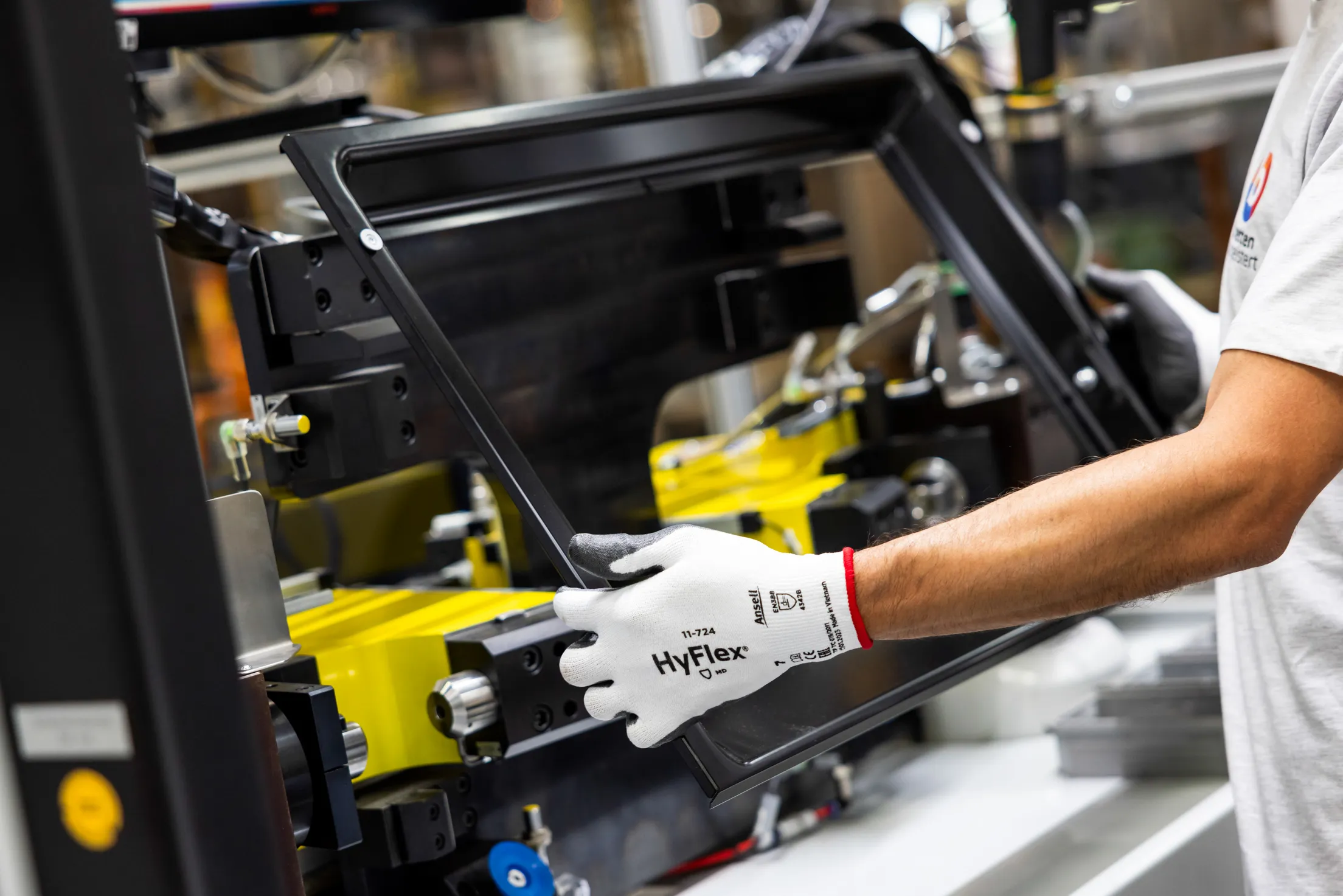 Ein Closeup auf zwei Arme und Hände mit weißen Sicherheitshandschuhen die eine schwarze Ofentür ohne Glas in den Händen halten. Das Foto ist in der Fertigung aufgenommen und die Ofentür wird gleich montiert. Im Vordergrund scharf ist die linke Hand des Mitarbeiters.