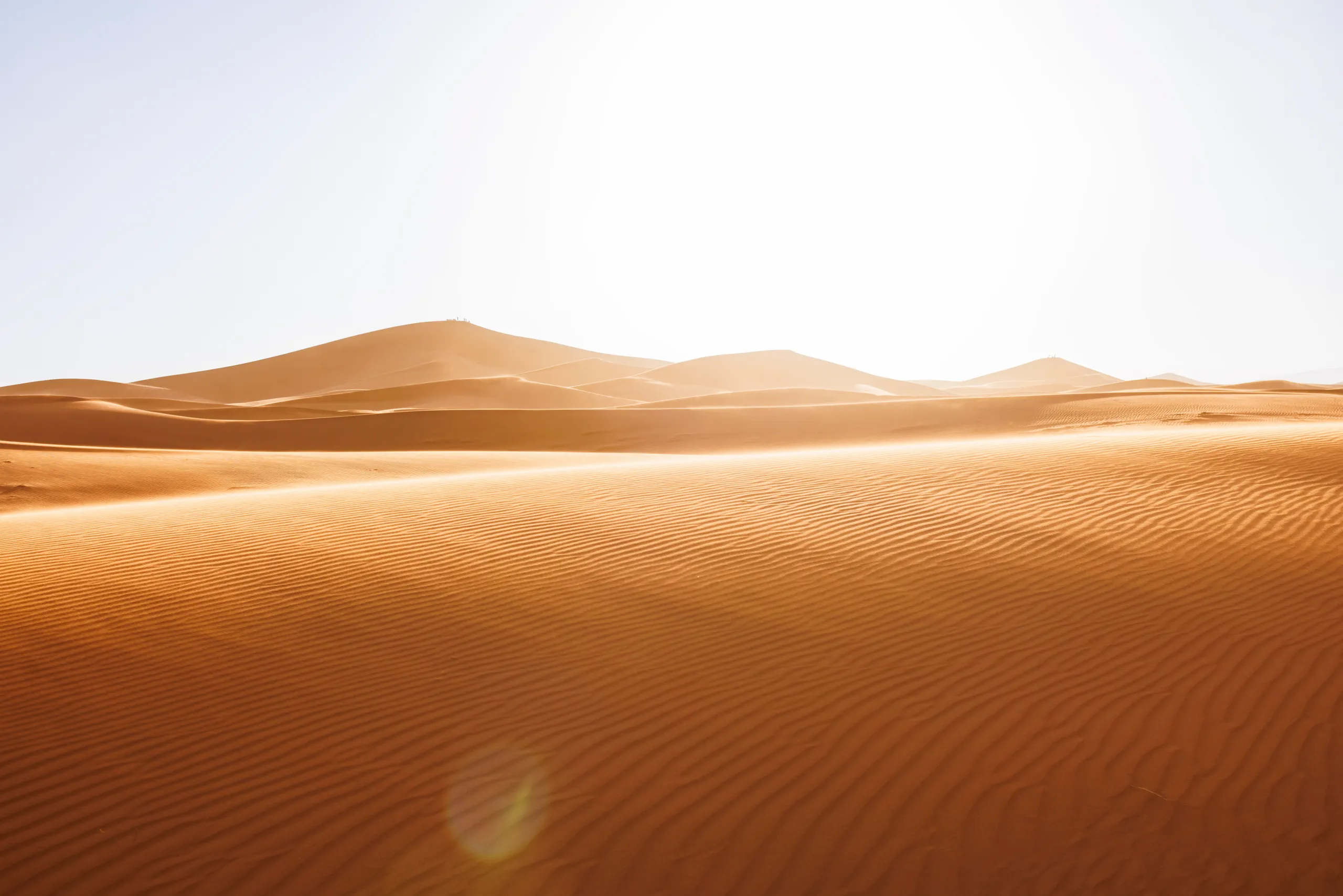 Ein Blick auf die Wüste Erg Chegaga bei untergehenden Sonne. Es ist eine Weitwinkelaufnahme mit vielen braunen Sanddünen zu sehen. Ein Lichtstreifen fällt auf den Sand.