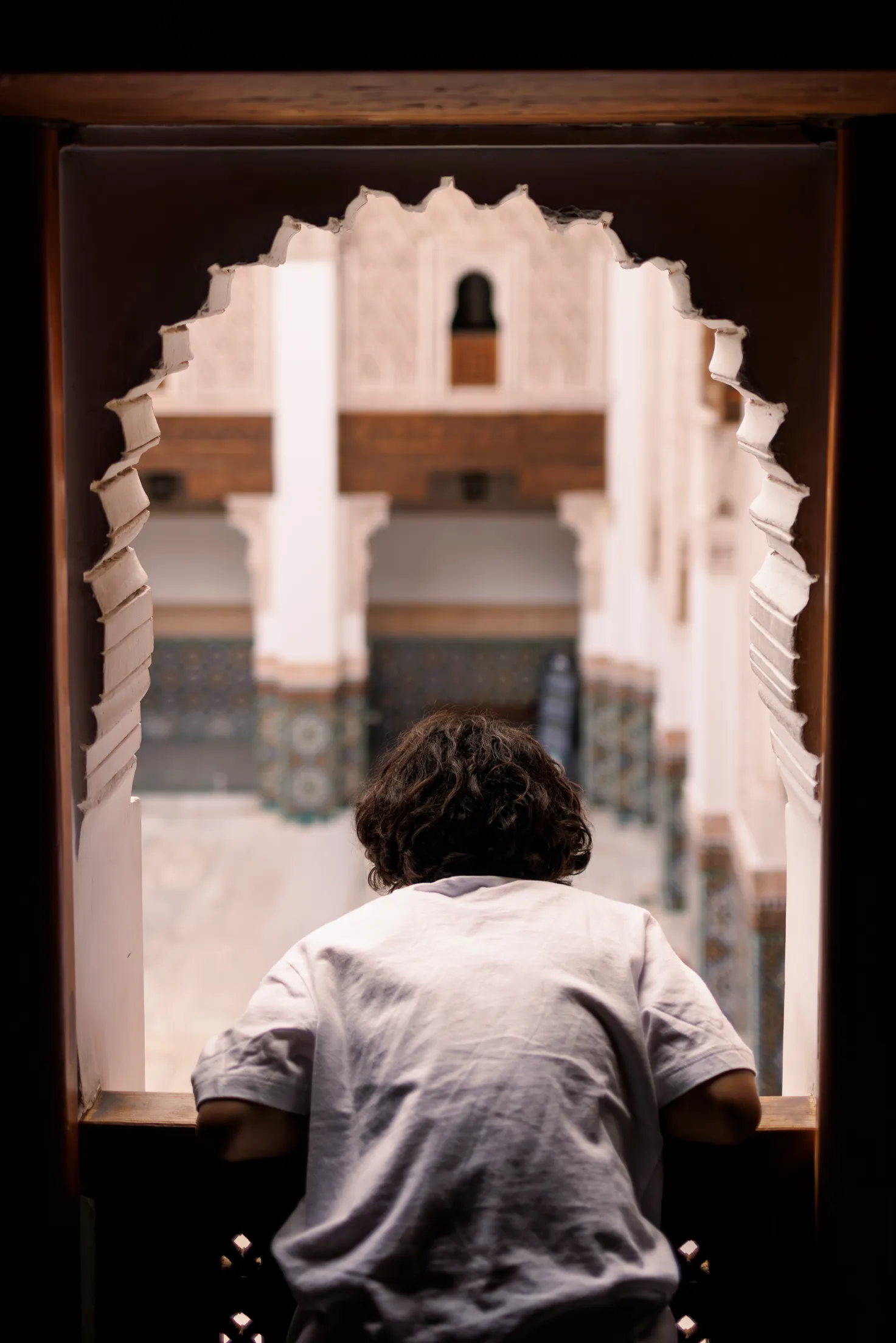 Aus einem Fenster in der Ben Youssef Moschee lehnt sich ein marrokanischer Junge mit weißem T-Shirt und schaut in den Hinterhof der Koranschule.