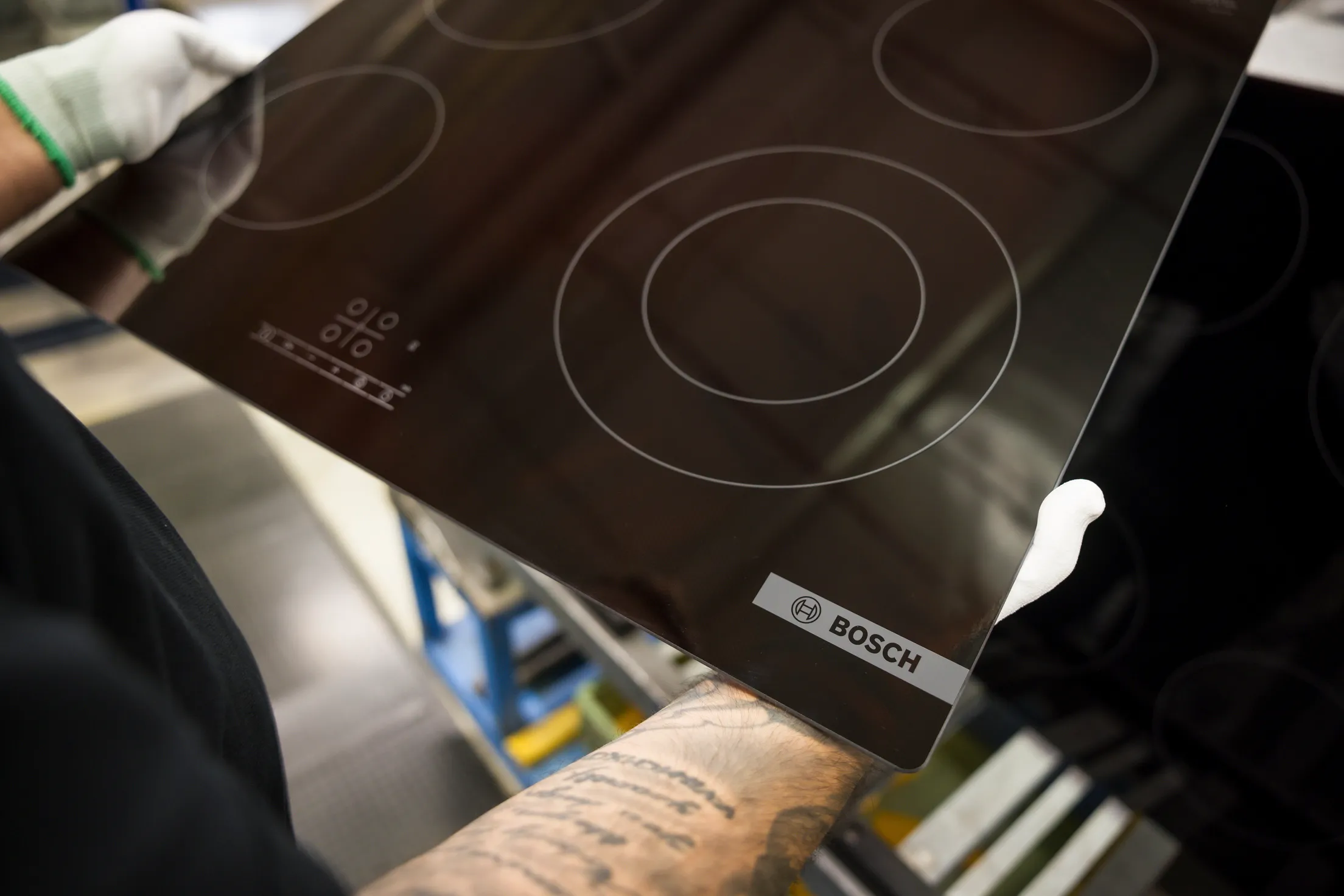 Detailaufnahme von einem schwarzen Cerankochfeld mit BSH Logo. Es wird von einem Mann mit weißen Handschuhen gehalten.